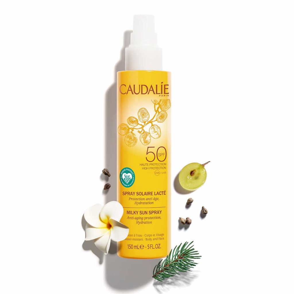 Sarı Caudalie SPF 50 güneş kremi şişesi, üzüm, çiçek ve çam dalları
