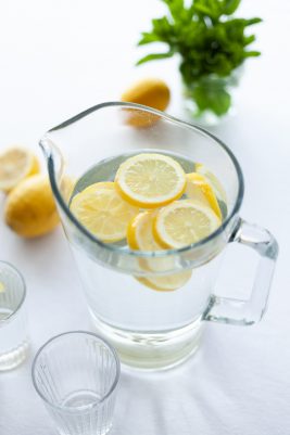 Sürahi içinde limon dilimli su, yanında limonlar ve nane yaprakları