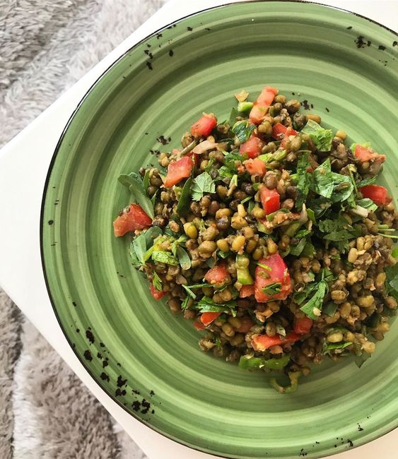 Yeşil tabakta mercimek, domates ve otlarla yapılmış salata