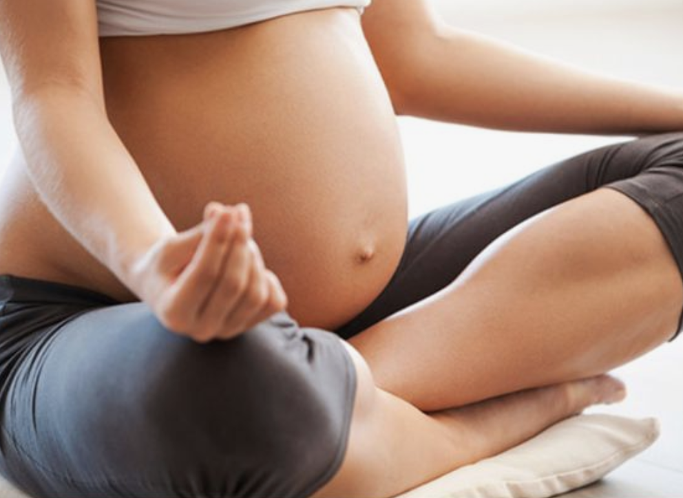 Hamile bir kadın meditasyon veya yoga yaparken bağdaş kurmuş oturuyor
