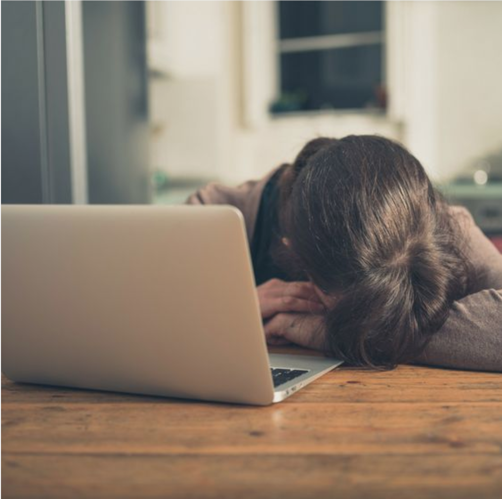 Dizüstü bilgisayarın yanında masaya başını koymuş yorgun kişi