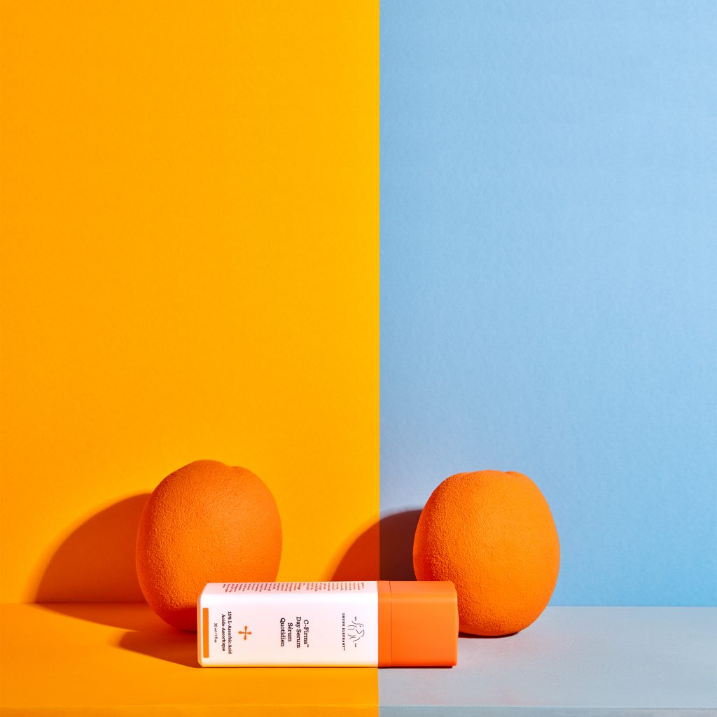 Drunk Elephant C-Firma serum, turuncu-mavi fonda iki portakal arasında