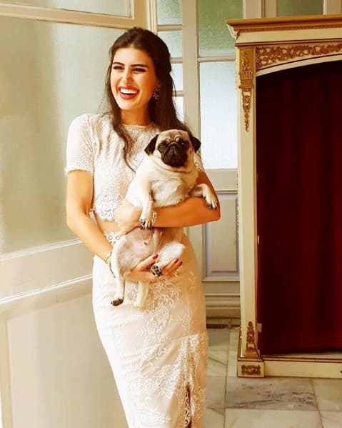 Gülümseyen kadın kucağında pug köpeğiyle beyaz dantel elbise içinde