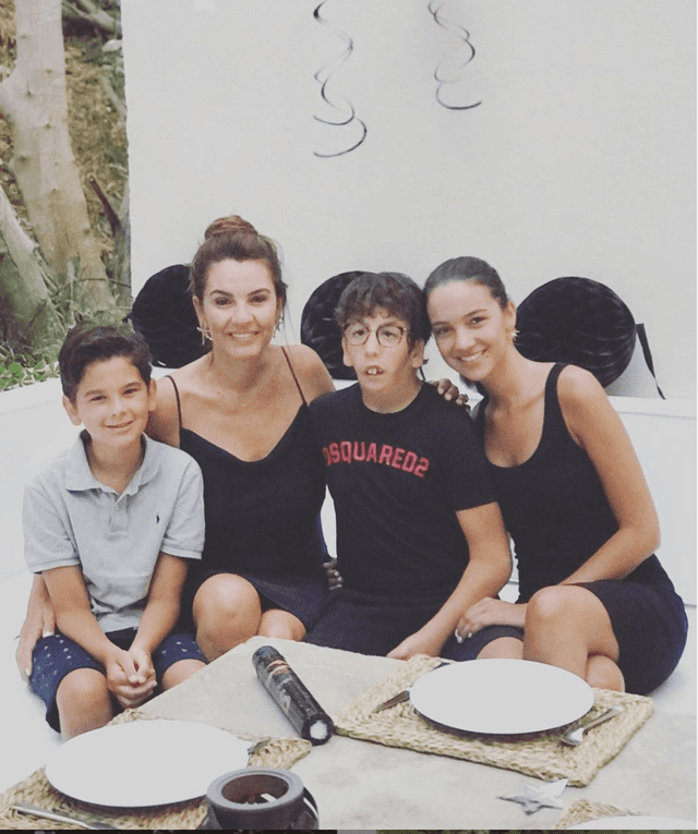 Mutlu bir aile masada oturmuş, gülümseyen anne ve üç çocuğu