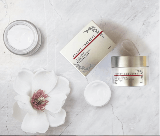 Probiyotikli Beauty Omelette yüz kremi kutusu ve kavanozları mermer üzerinde