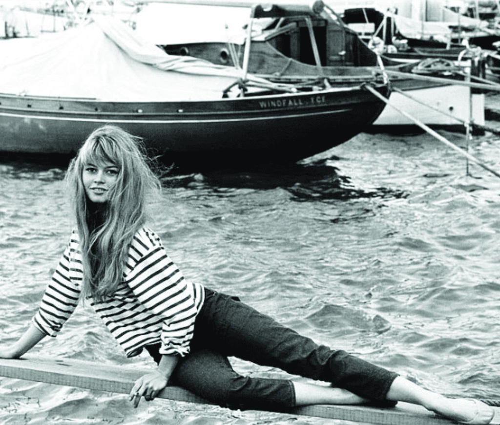 Bridget Bardot çizgili tişörtle su kenarında uzanmış, arkada tekneler