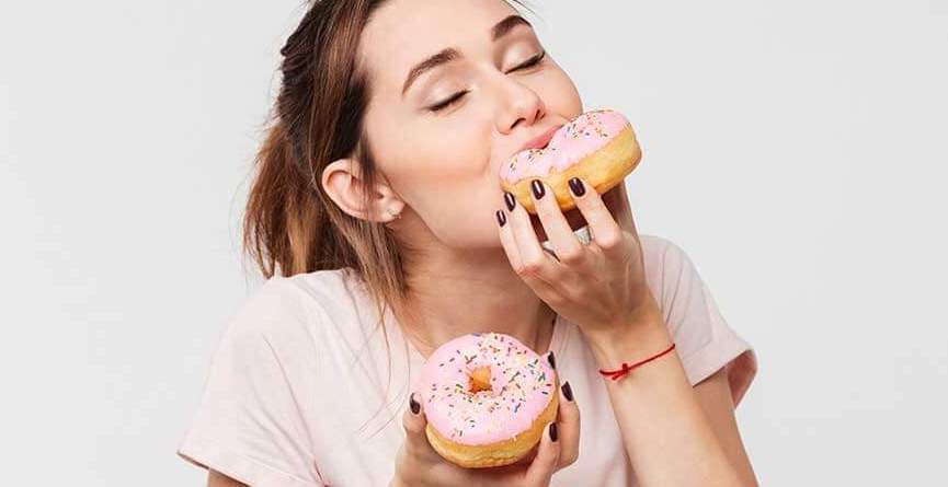 Pembe donut yiyen ve keyif alan mutlu genç kadın