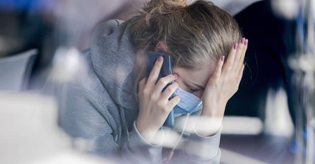 Maskeli kadın telefonla konuşurken başını tutmuş, stresli ve endişeli