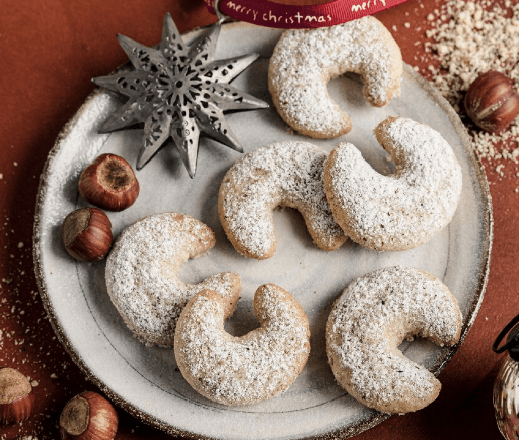 Pudra şekerli hilal kurabiyeler, fındık ve noel süsleriyle tabakta