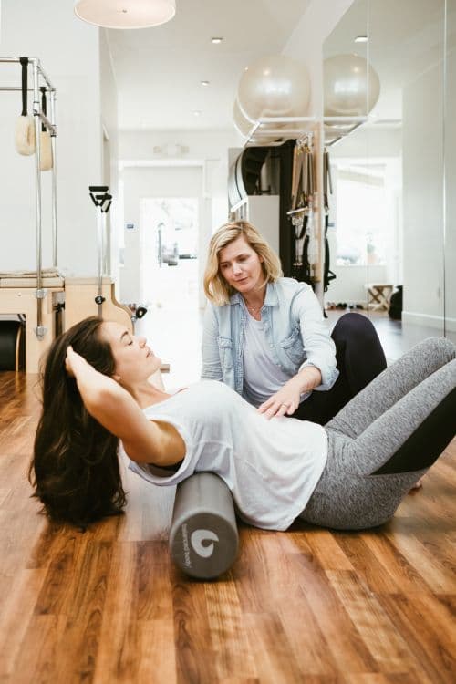 Pilates stüdyosunda köpük rulo ile egzersiz yapan kadın ve eğitmeni