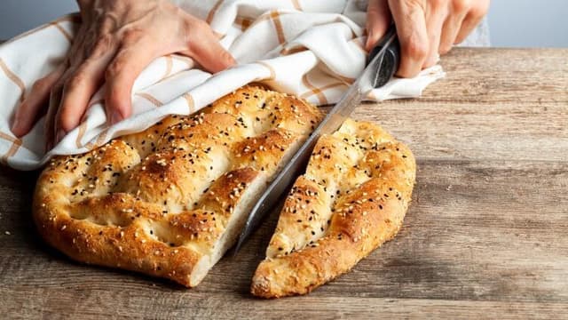 Susamlı Ramazan pidesi ahşap bir masa üzerinde elle kesiliyor