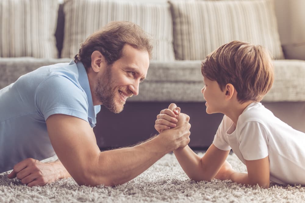 Baba ve oğul halıda kol güreşi yaparken gülümsüyorlar