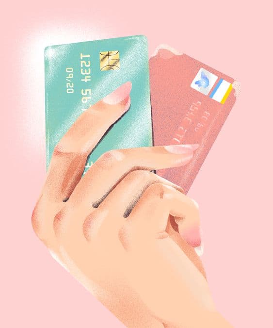 Pembe zeminde bir el turkuaz ve pembe iki kredi kartı tutuyor