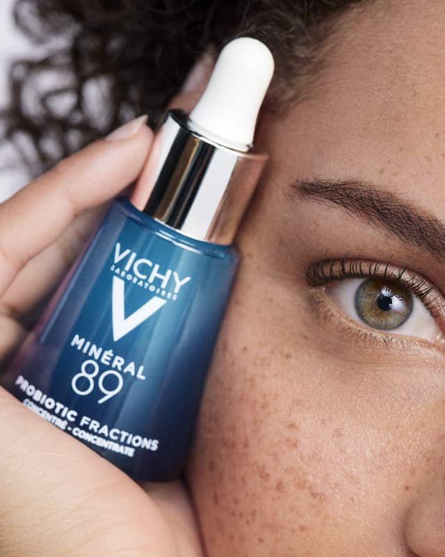 Elinde Vichy Mineral 89 serum şişesi tutan çilli bir kadın yüzü ve gözü