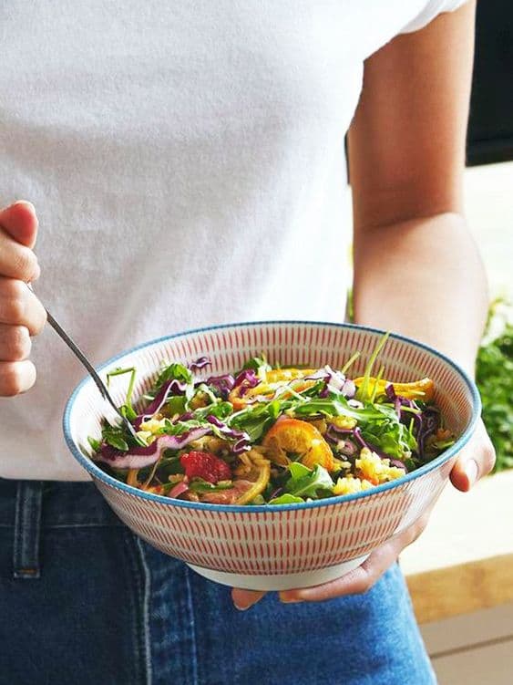 Taze renkli salata kasesinden çatalıyla yiyen beyaz tişörtlü kişi