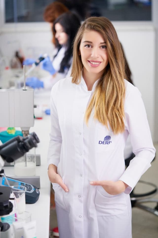 Laboratuvar önlüklü genç bir kadın laboratuvarda gülümseyerek poz veriyor
