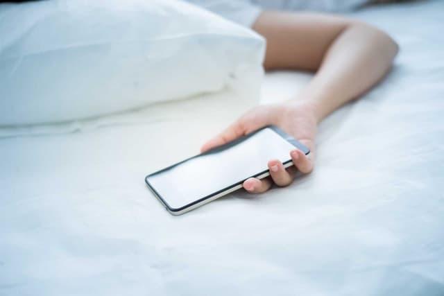 Yatakta yatan kişinin elinde duran akıllı telefon
