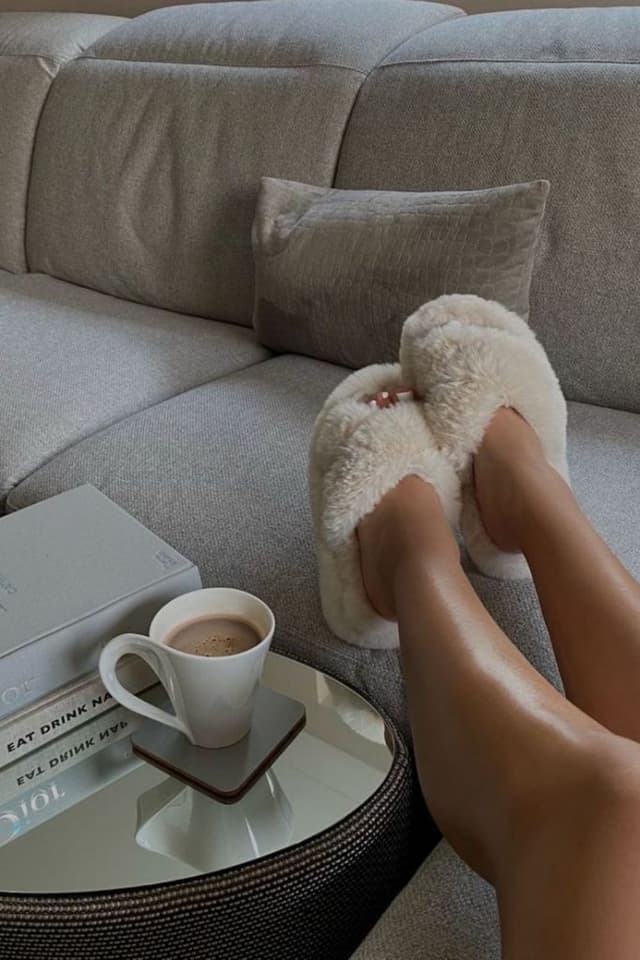 Peluş terlikli ayaklar, gri koltukta kahve ve kitaplar
