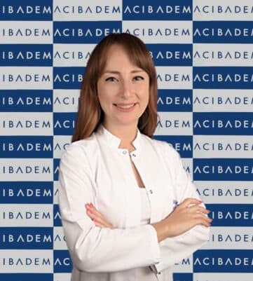 Acıbadem logosu önünde beyaz önlüklü gülümseyen kadın doktor