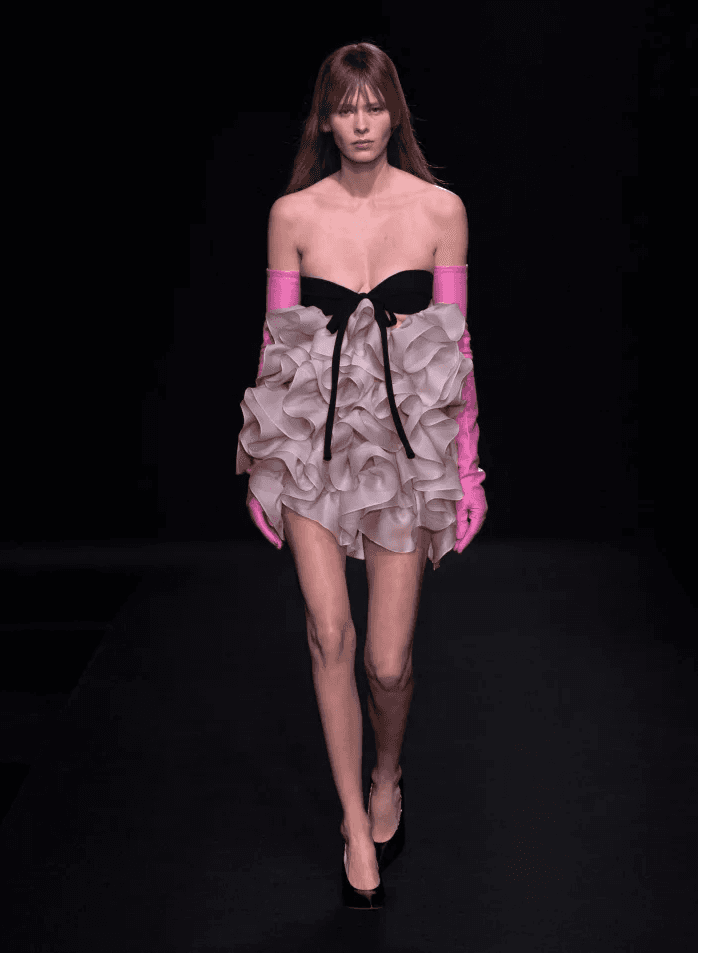 Model pembe eldivenli, fırfırlı etekli askısız elbisesiyle podyumda