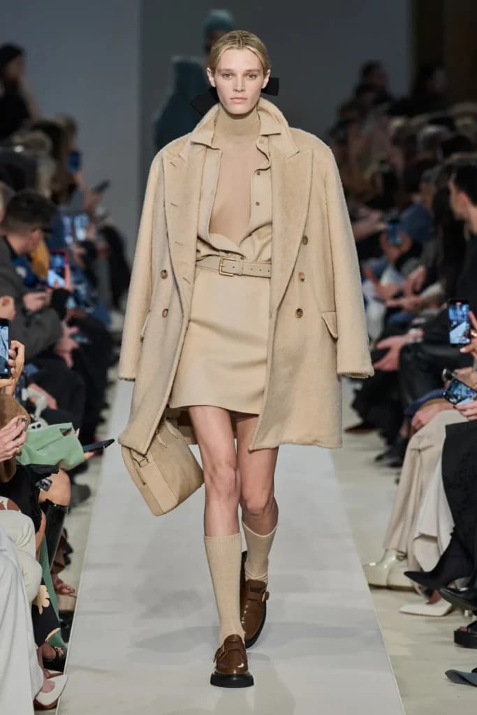 Moda defilesinde bej renkli palto ve kıyafet giyen bir model
