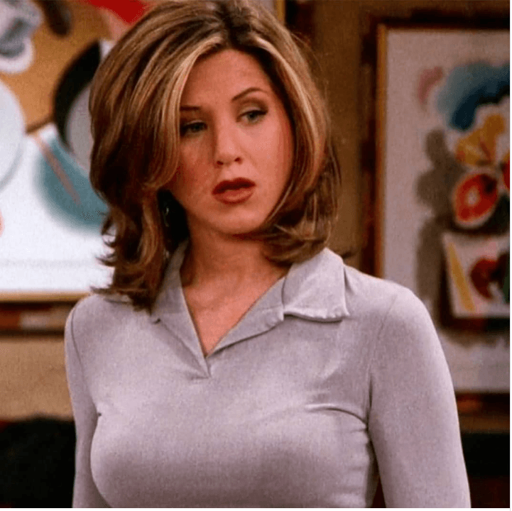 Rachel Green belirgin saç stili ve gri üstüyle düşenceli bakıyor