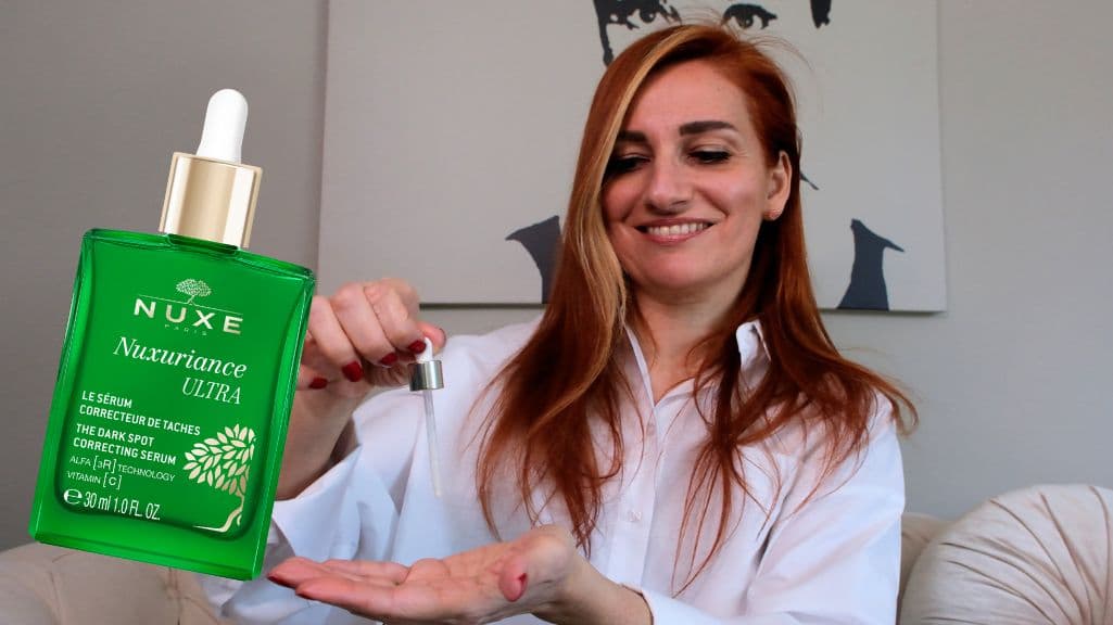 Gülümseyen kadın Nuxe Nuxuriance Ultra koyu leke serumunu eline damlatıyor
