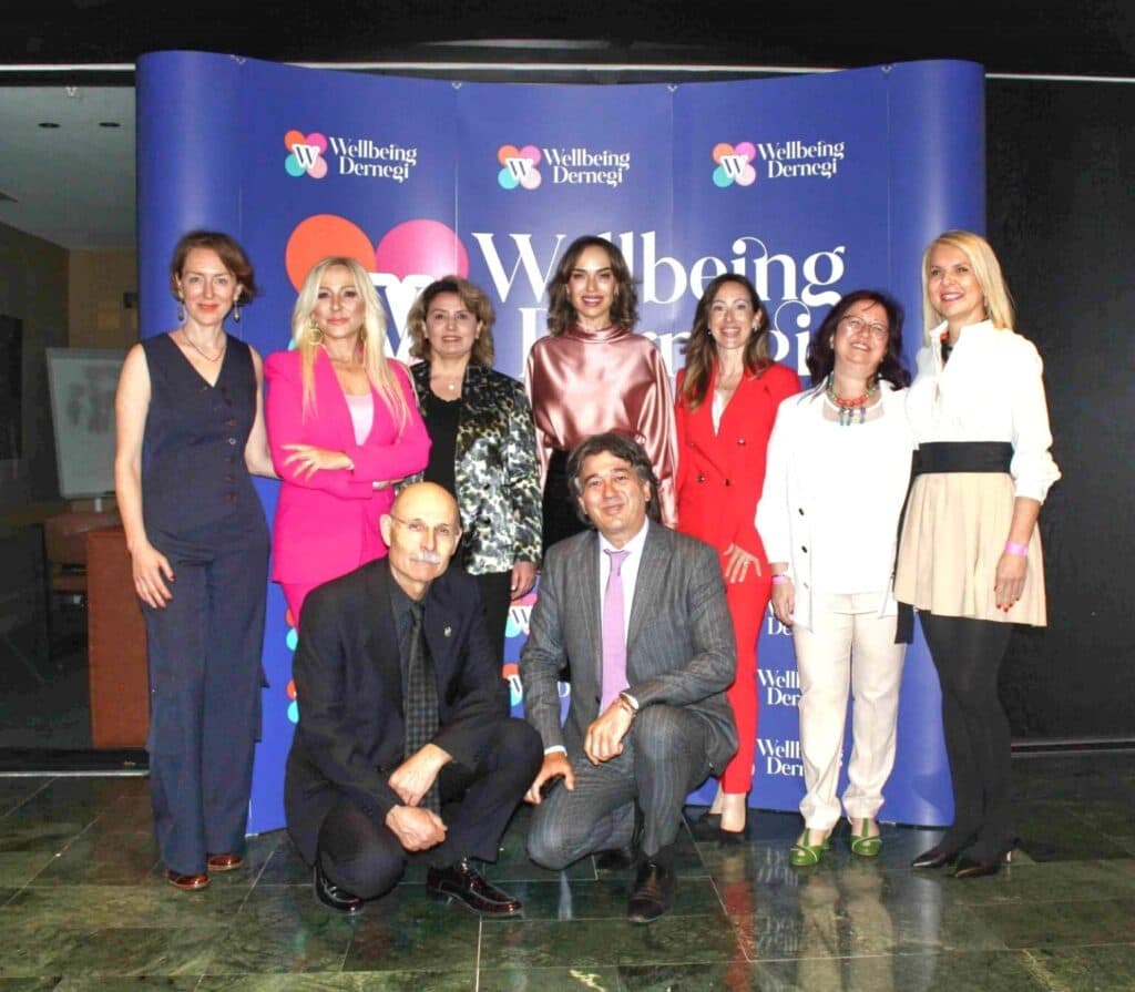 Wellbeing Dernegi etkinliğinde gülümseyen kadınlar ve erkekler grup pozu veriyor
