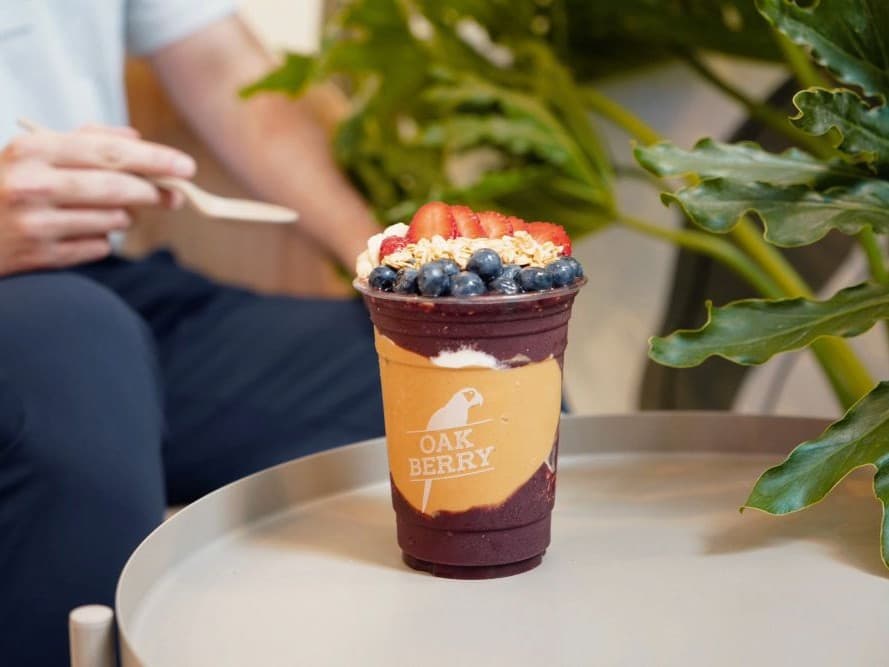 Oak Berry açaí bardağı meyveler ve granola ile bir kişi yanında