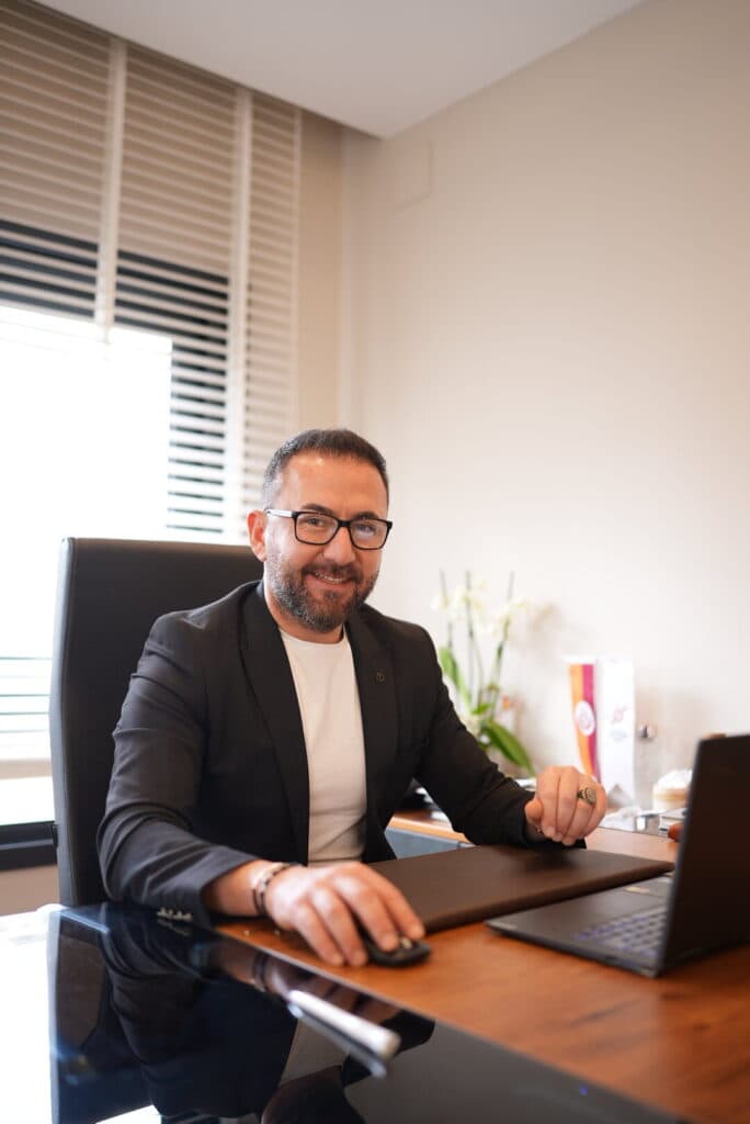 Gülümseyen gözlüklü takım elbiseli iş adamı ofis masasında laptop kullanıyor