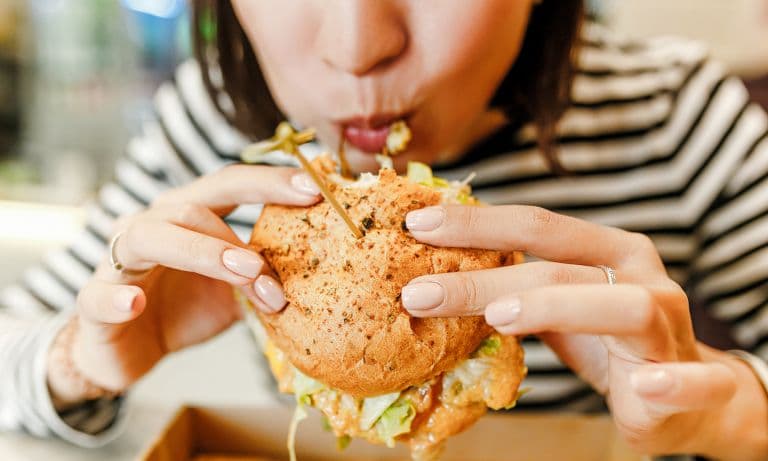 Çizgili bluzlu bir kadın büyük bir hamburgeri iştahla ısırıyor