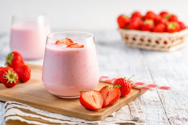 Pembe çilekli smoothie, taze çilekler ve pipetler ahşap bir tepside