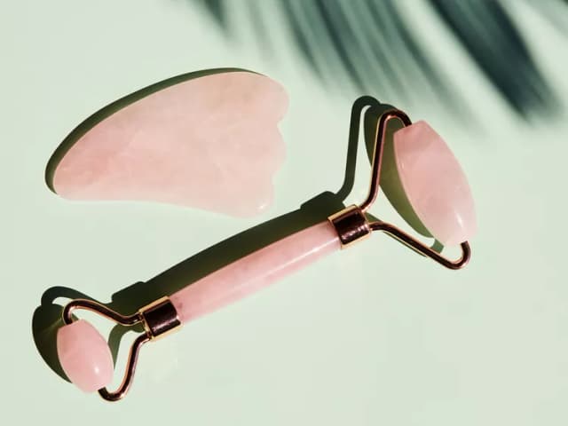 Pembe kuvars gua sha ve yüz rulosu, gölgeli açık yeşil zeminde