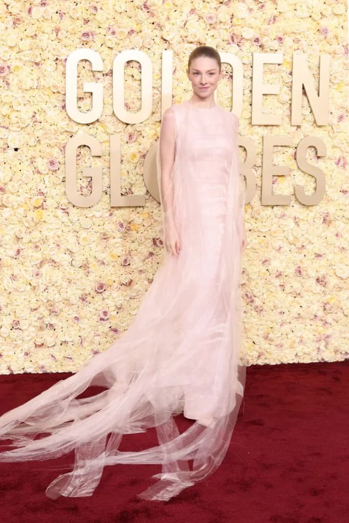 Kırmızı halıda şeffaf pembe elbise giyen kadın Golden Globes logosu önünde