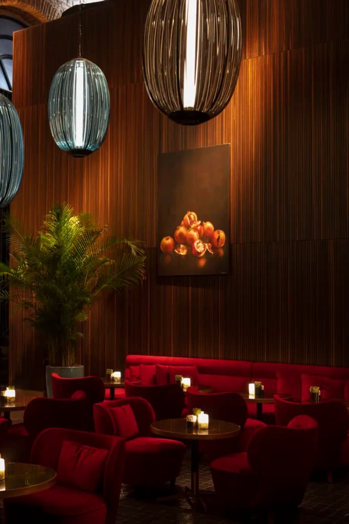Kırmızı koltuklu, ahşap duvarlı, modern avizeli ve bitkili loş bir bar