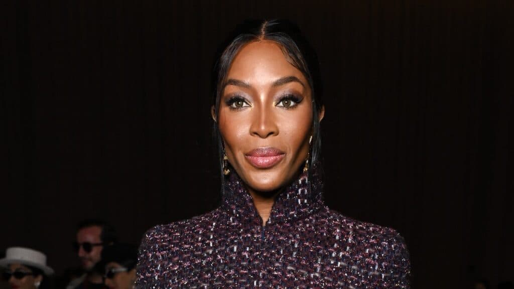 Naomi Campbell koyu renkli, dokulu bir ceketle doğrudan kameraya bakıyor