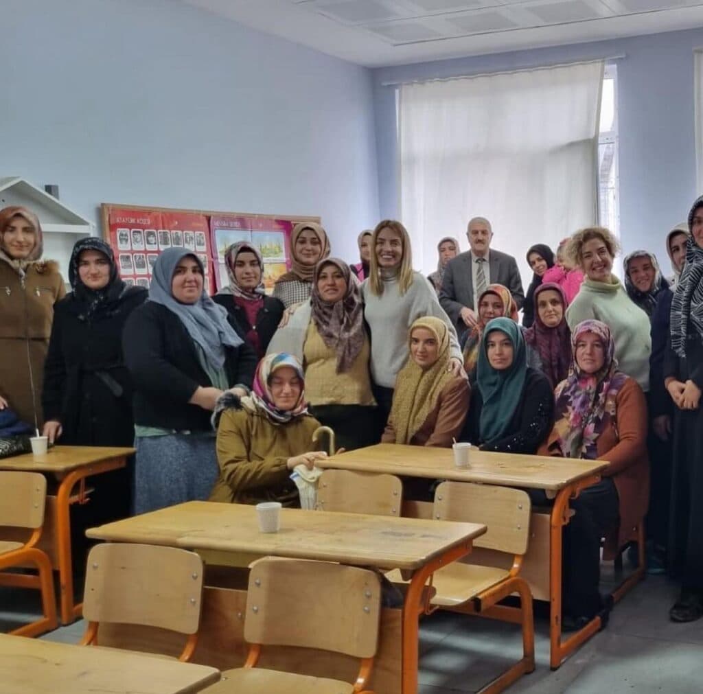 Sınıfta başörtülü kadınlar ve bir erkek kameraya gülümsüyor