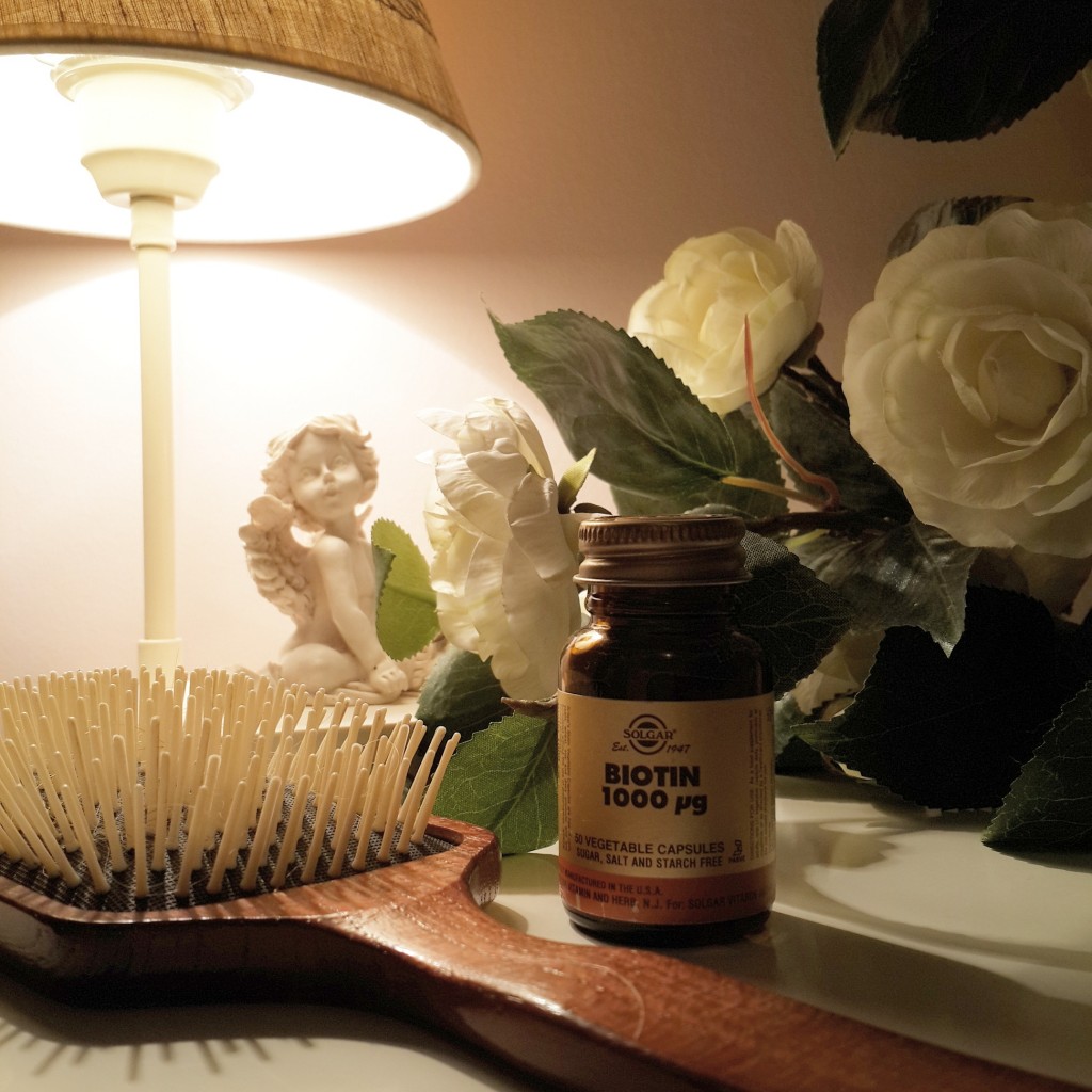 Biotin şişesi, ahşap saç fırçası, lamba, melek figürü ve beyaz çiçekler