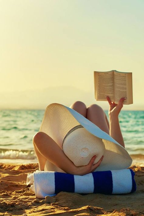 Hasır şapkalı bir kadın kumsalda uzanmış kitap okuyor