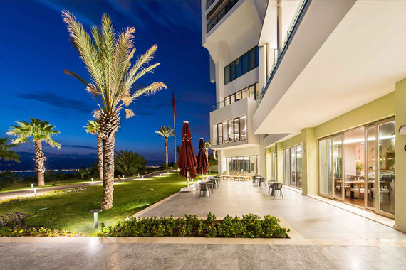 Gece aydınlatmalı palmiyeler, otel bahçesi ve teras alanı deniz manzarasıyla