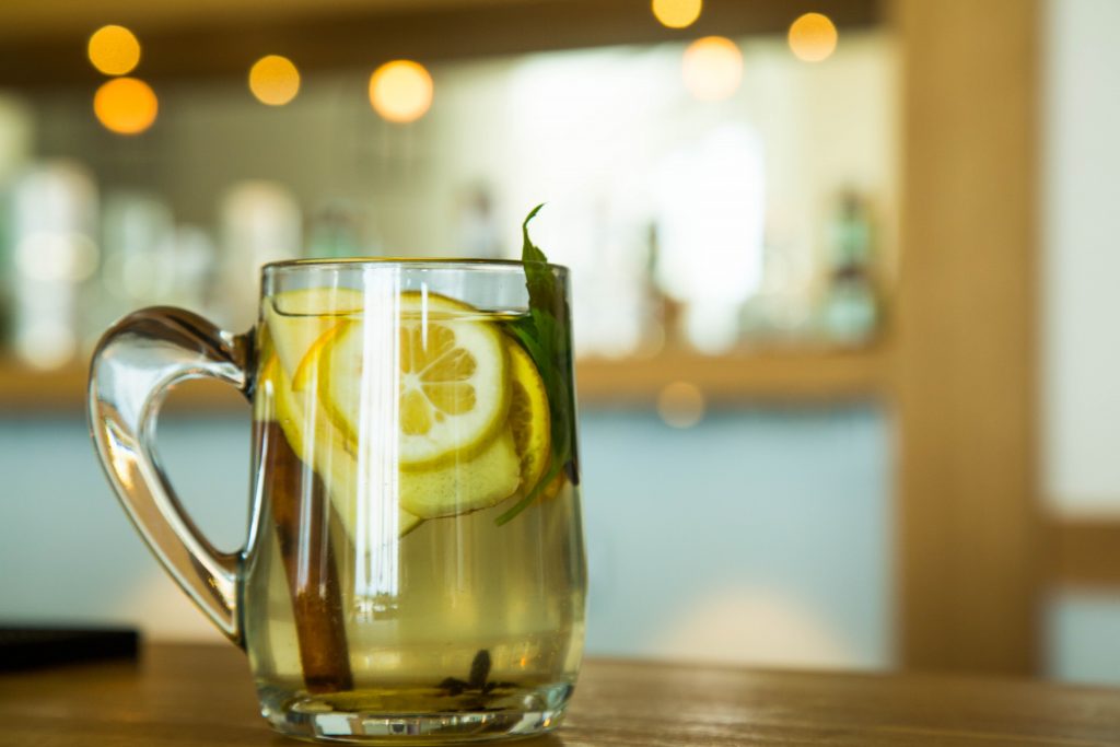 Limon dilimli tarçın çubuklu yeşil yapraklı cam kupa içeceği