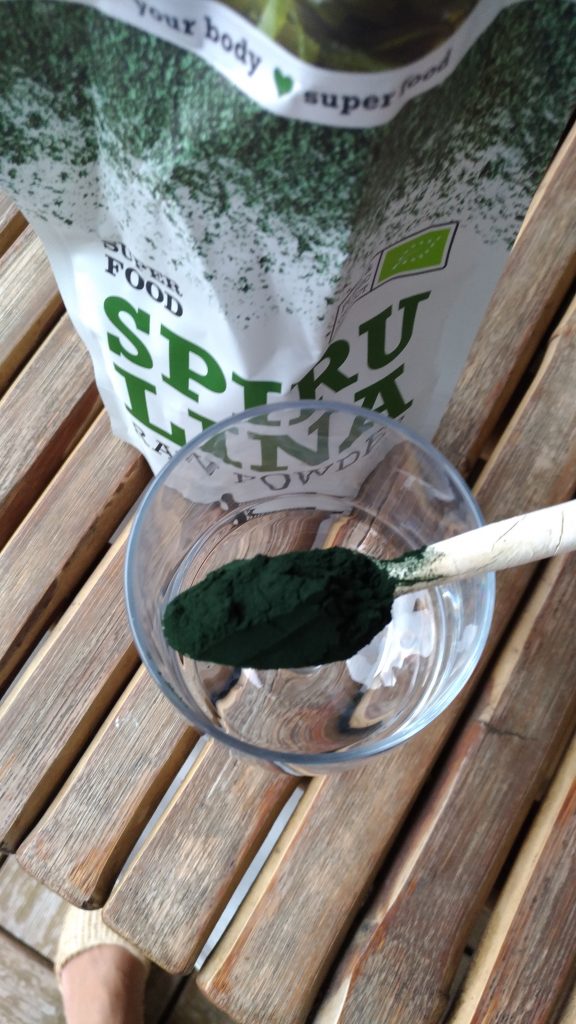 Ahşap masada kaşıkta yeşil spirulina süper gıda tozu ve paketi
