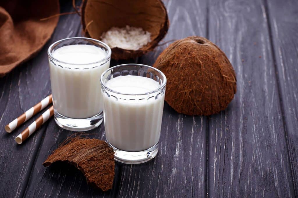 Koyu ahşap masa üzerinde iki bardak hindistan cevizi sütü ve meyvesi