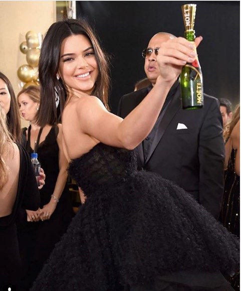Kendall Jenner siyah elbisesiyle mini şampanya tutuyor gülümsüyor