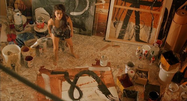 Dağınık sanat atölyesinde boyalarla kaplı bir kadın