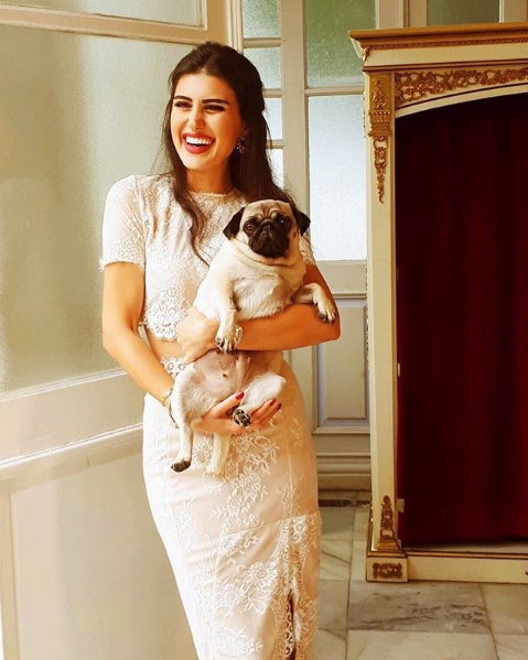 Gülümseyen kadın kucağında pug köpeğiyle beyaz dantel elbise içinde