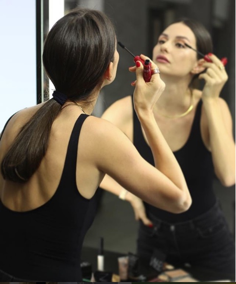 Aynada maskara süren, sırtı dönük genç bir kadın
