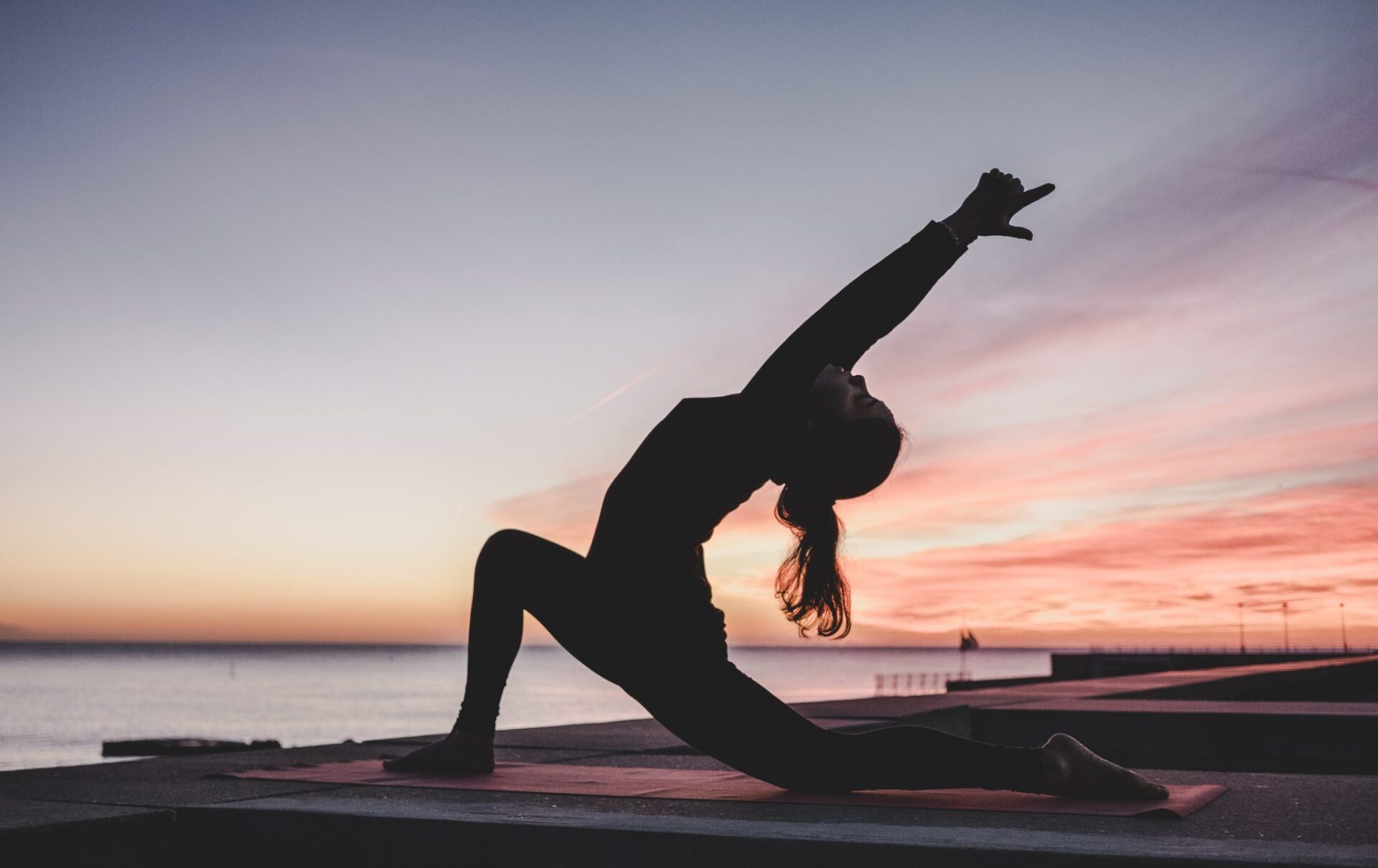 Gün batımı deniz kenarında yoga pozu veren kadının silueti
