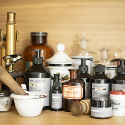 Ahşap rafta eski eczane şişeleri, havan, mikroskop ve kozmetik ürünler