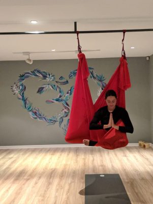 Hava yogası yapan kadın kırmızı hamakta meditasyon pozisyonunda Om sembolü